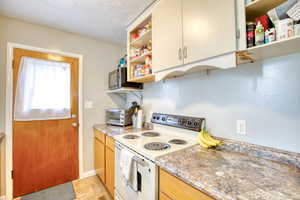 Kitchen featuring white range with electric stovetop, open shelves, and black microwave