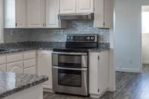 Kitchen featuring dark stone counters, double oven range, white cabinetry, and dark wood-style flooring