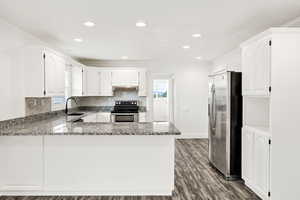 Kitchen with a peninsula, stainless steel appliances, white cabinets, dark wood-style flooring, and dark stone counters