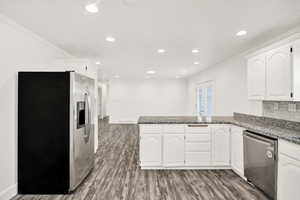 Kitchen with stainless steel appliances, a peninsula, dark stone counters, ornamental molding, and recessed lighting