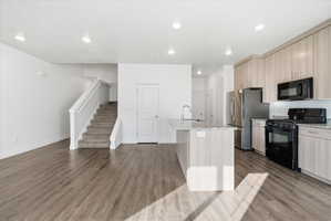 Kitchen featuring black appliances, light stone countertops, light wood finish cabinets, a center island with sink, and recessed lighting