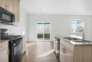 Kitchen featuring black appliances, light stone countertops, light wood finish cabinetry, and recessed lighting