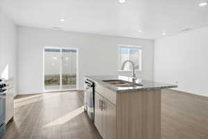 Kitchen with light stone counters, dark wood-style flooring, a center island with sink, modern cabinets, and recessed lighting