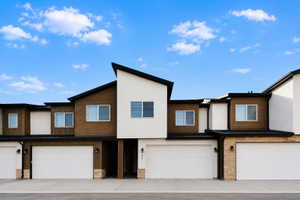 Modern townhome exterior featuring contemporary architectural lines, a striking combination of white stucco and dark wood-finish siding, multiple windows, an attached two-car garage, and stone accents