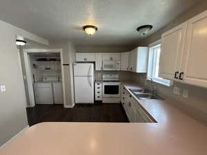 Kitchen featuring white cabinetry, white appliances, light countertops, washer and dryer, and dark wood-style floors