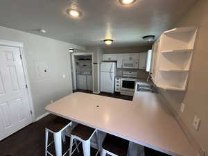Kitchen with light countertops, white appliances, open shelves, a peninsula, and a textured ceiling
