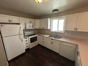 Kitchen with white cabinets, light countertops, white appliances, and a textured ceiling