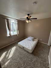 Bedroom with dark colored carpet, a ceiling fan, and a textured ceiling