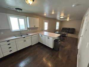 Kitchen featuring light countertops, a textured ceiling, a peninsula, white dishwasher, and white cabinetry