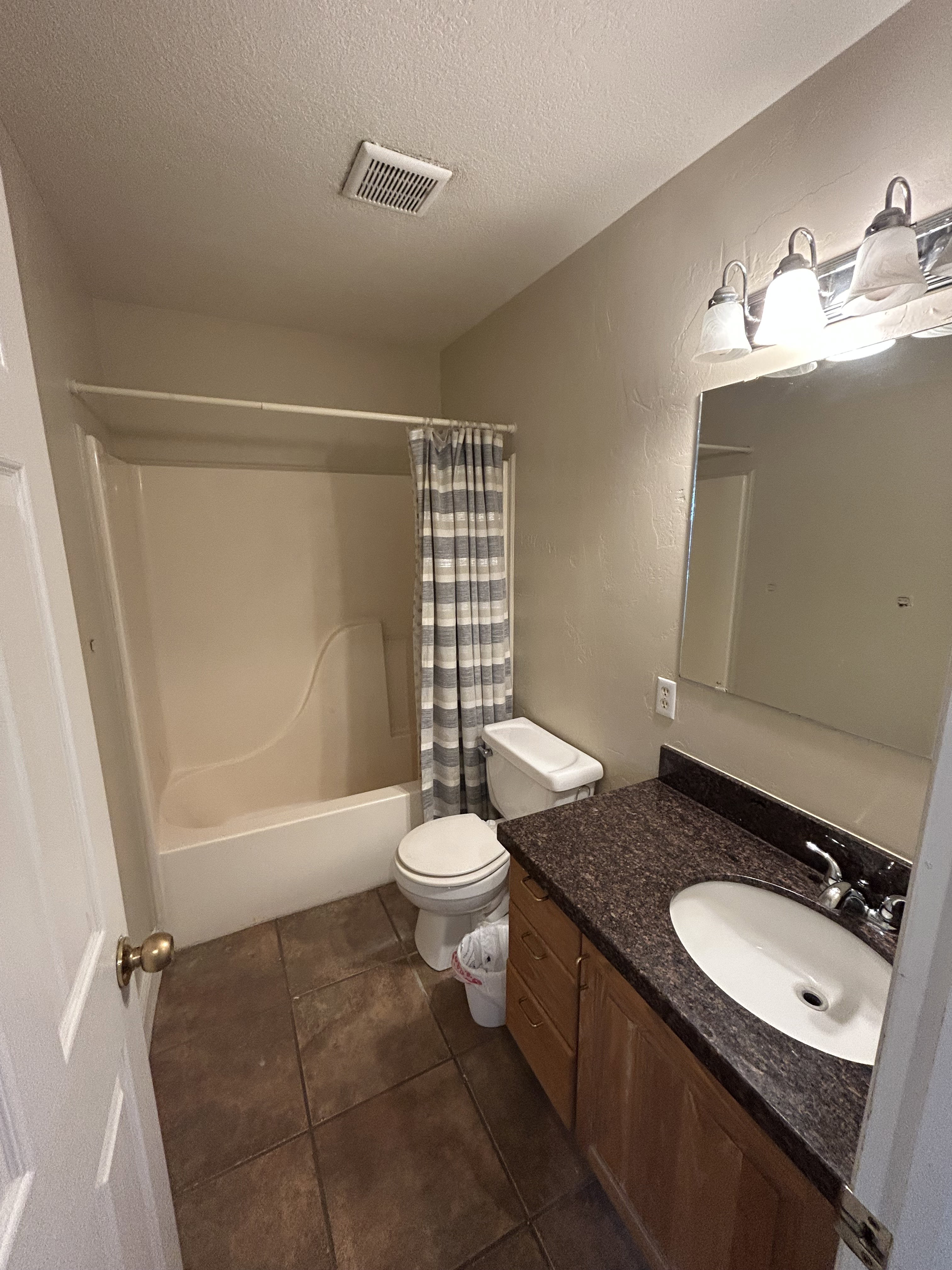 Bathroom featuring vanity, a textured ceiling, shower / bath combo, dark tile patterned flooring, and a textured wall