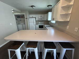 Kitchen featuring a kitchen bar, light countertops, washer and clothes dryer, white appliances, and a peninsula