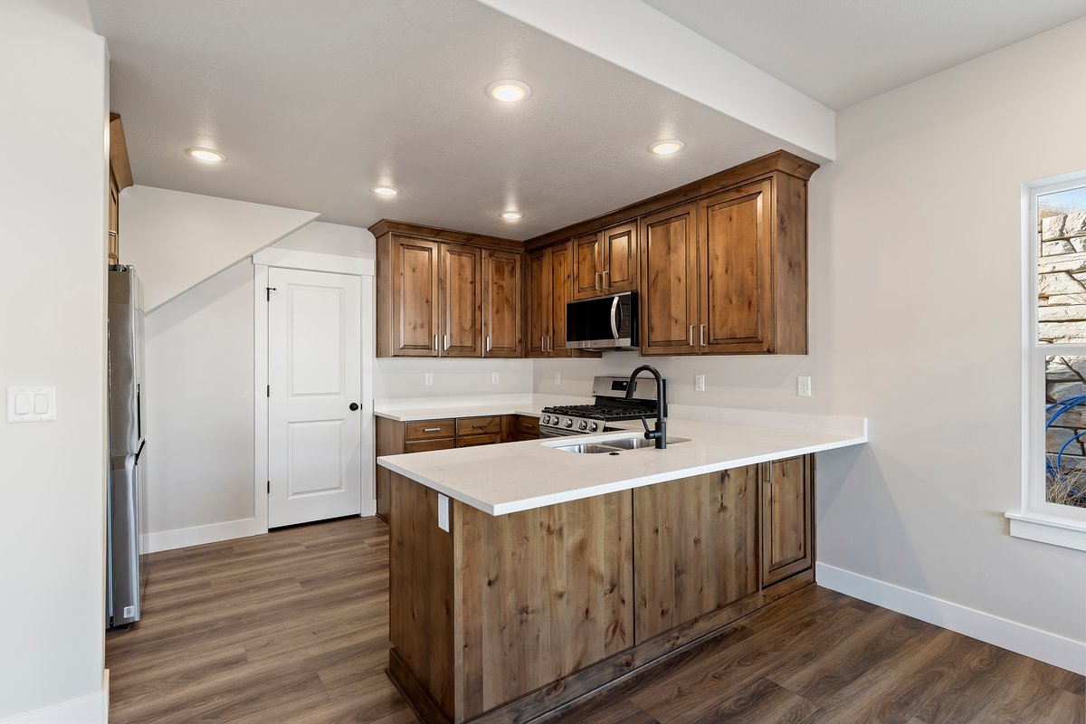Kitchen featuring dark wood-type flooring, a peninsula, wood finish cabinets, stainless steel appliances, and recessed lighting