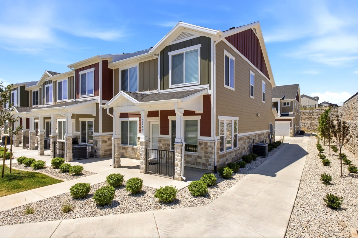 Modern townhome exterior featuring multi-toned siding, stone accents, white trim, and a covered porch