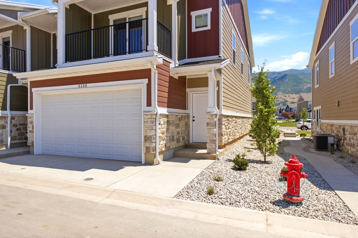 Multi-story residence featuring a two-car garage with a panel door, stone veneer skirting, and a second-story balcony with dark railings