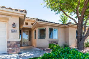 Doorway to property featuring stucco siding, a tile roof, stone siding, and a garage
