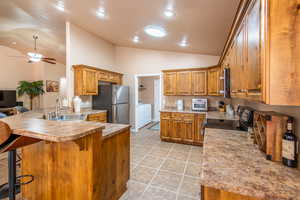 Kitchen with wood finish cabinets, a peninsula, lofted ceiling, a breakfast bar, and light countertops