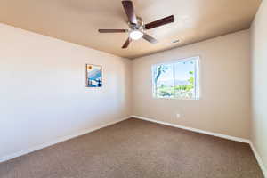 Empty room featuring a ceiling fan and dark colored carpet