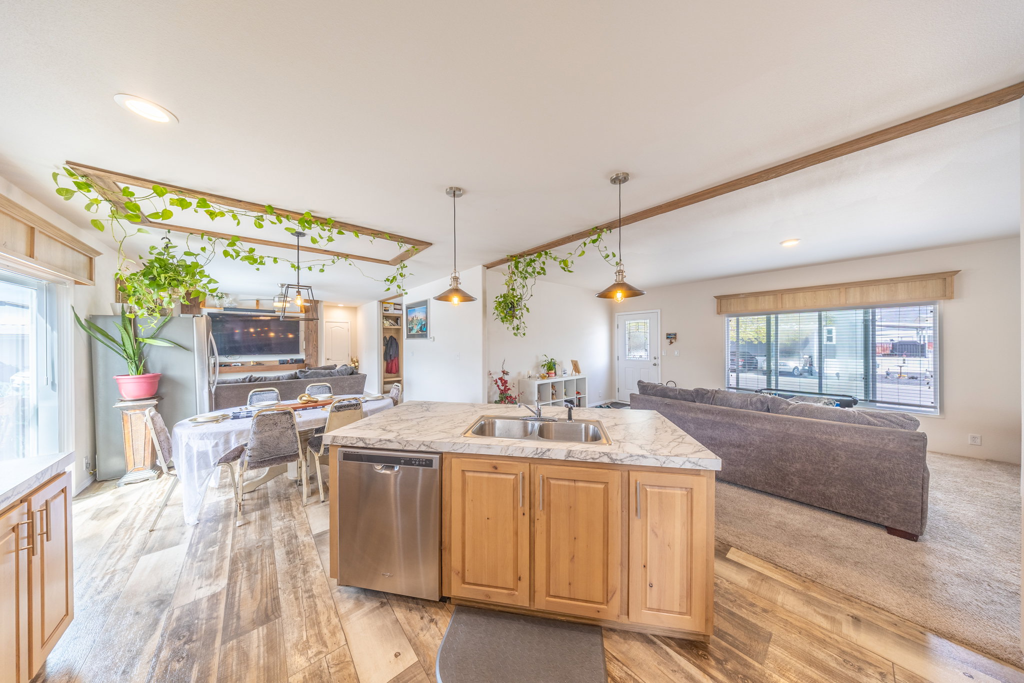 Kitchen featuring light countertops, open floor plan, a center island with sink, dishwasher, and hanging light fixtures