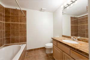 Full bath with a textured ceiling, vanity, dark tile patterned floors, and tiled shower / bath combo