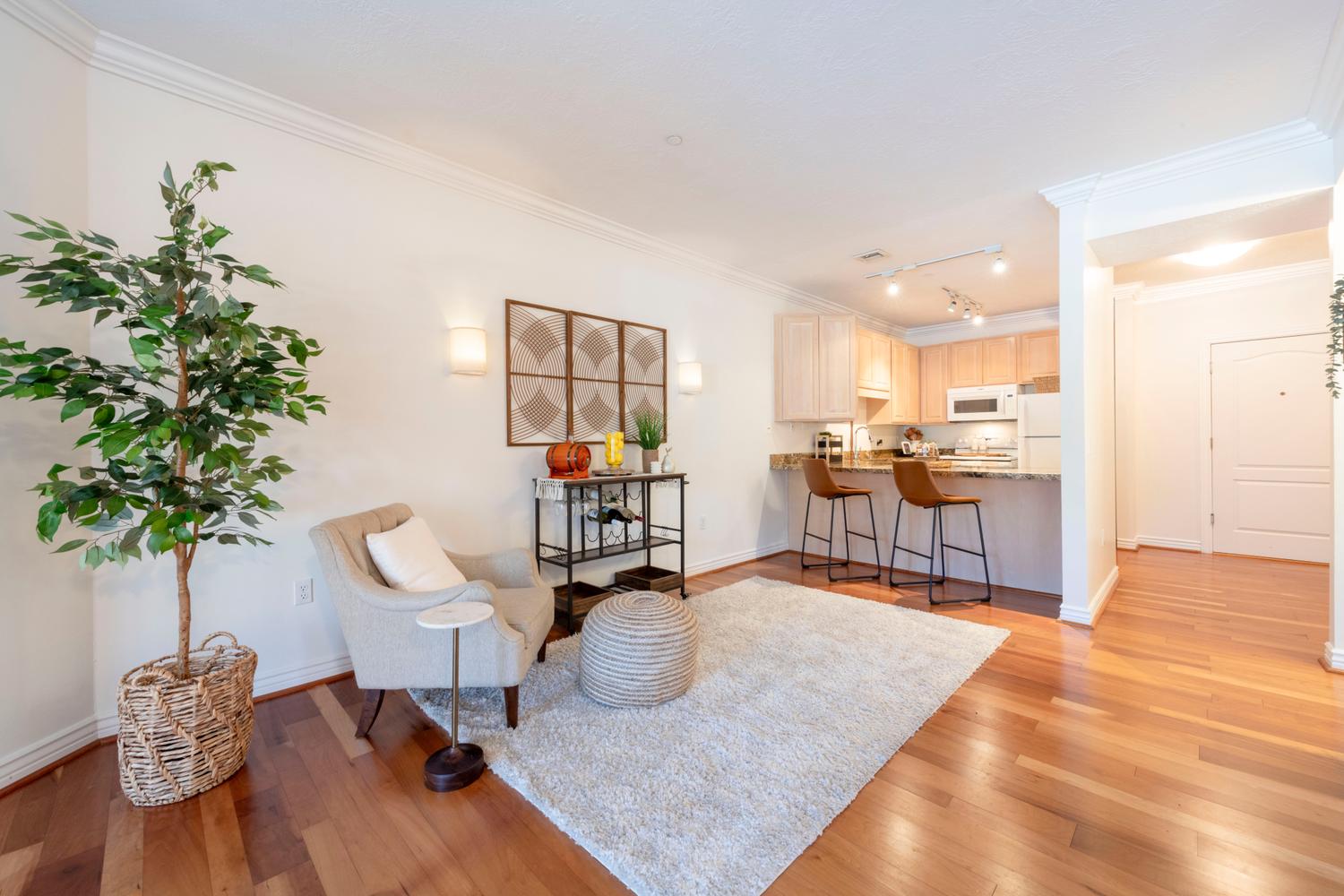 Open-concept living area featuring wood-finish flooring, crown molding, and a kitchen pass-through with a stone countertop