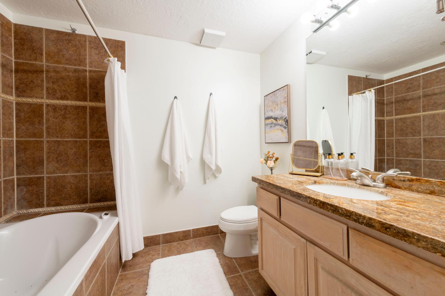 Bathroom featuring a single vanity with an integrated sink, a tiled tub-shower combination, a large wall-mounted mirror, and tile flooring
