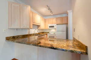 Kitchen with light wood finish cabinetry, white appliances, dark stone counters, rail lighting, and a peninsula