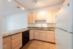 Kitchen featuring freestanding refrigerator, light wood finish cabinets, crown molding, dark stone countertops, and dishwasher