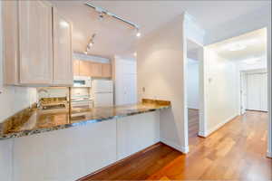 Kitchen featuring light wood-style flooring, light wood finish cabinetry, white appliances, rail lighting, and ornamental molding
