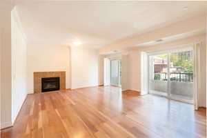 Unfurnished living room with crown molding, light wood-type flooring, and a tiled fireplace
