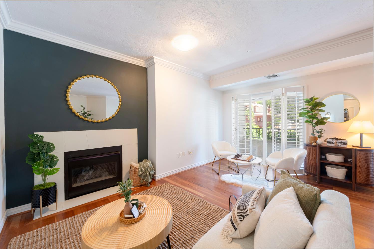 Living area featuring a fireplace with a light-toned surround, hardwood flooring, crown molding, and a balcony entrance with plantation shutters