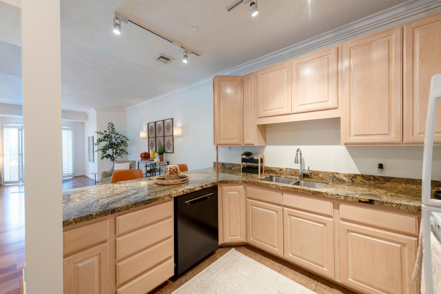 Kitchen featuring light wood cabinetry, granite-style countertops, double basin stainless steel sink, and a built-in black dishwasher