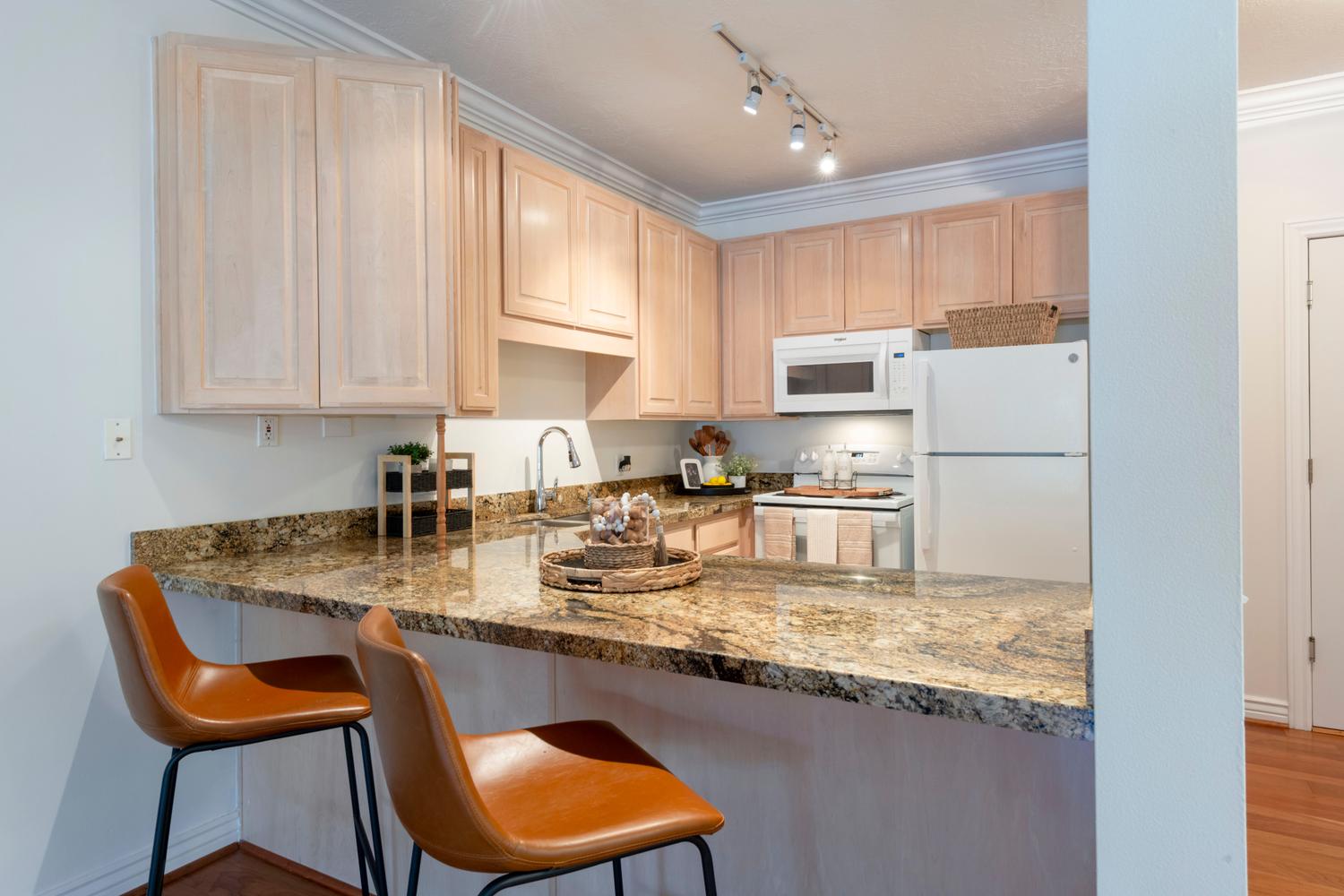 Kitchen featuring a granite countertop breakfast bar, wood-finish cabinetry, built-in microwave, and track lighting