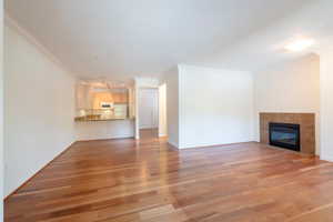Unfurnished living room with ornamental molding, light wood-style floors, and a tiled fireplace
