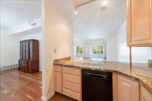 Kitchen featuring light wood finish cabinetry, black dishwasher, crown molding, dark stone countertops, and light wood finished floors