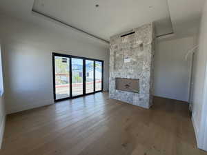 Unfurnished living room with a fireplace, a raised ceiling, and light wood-style flooring
