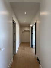 Hallway with light wood-type flooring, arched walkways, and recessed lighting