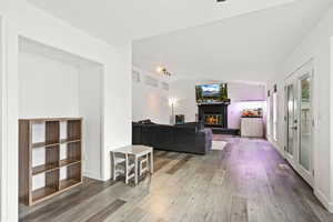 Living room featuring light wood-style floors, vaulted ceiling, and a glass covered fireplace