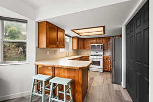Kitchen with wood finish cabinets, a peninsula, a kitchen bar, light countertops, and light wood-type flooring