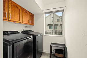 Laundry room with washing machine and clothes dryer, light wood-type flooring, and cabinet space