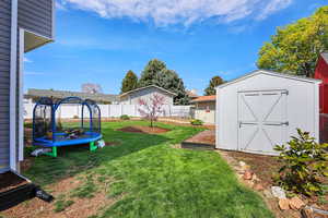 Fenced backyard featuring a trampoline and a storage shed