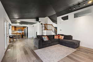 Living room featuring light wood finished floors, lofted ceiling, track lighting, and a ceiling fan
