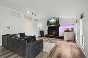 Living area featuring vaulted ceiling, rail lighting, light wood-style floors, and a brick fireplace