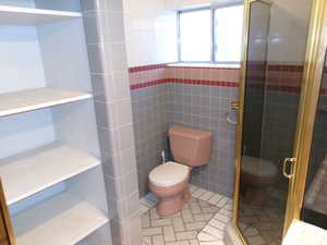Basement 3/4 bathroom with tile walls, a stall shower, and light tile patterned floors