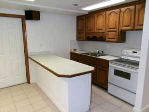 Basement Kitchen featuring white range with electric stovetop, light countertops, wood finish cabinetry, and a peninsula