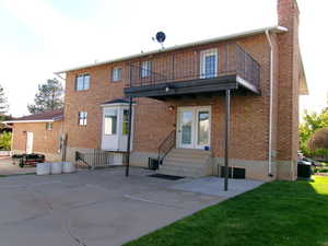 Back of house with a balcony, brick siding, a chimney, and entry steps