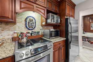 Kitchen with stainless steel appliances, light stone counters, light tile patterned floors, and backsplash