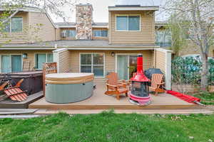 Back of house with a hot tub, a shingled roof, a wooden deck, and a chimney