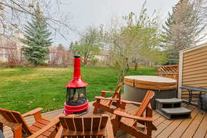 Wooden terrace with a hot tub, a yard, and a fire pit