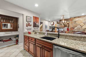 Kitchen featuring light stone counters, hanging lights, dishwasher, wood finish cabinetry, and light tile patterned flooring