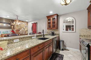 Kitchen featuring glass fronted cabinets, stainless steel appliances, light tile patterned floors, light stone counters, and backsplash